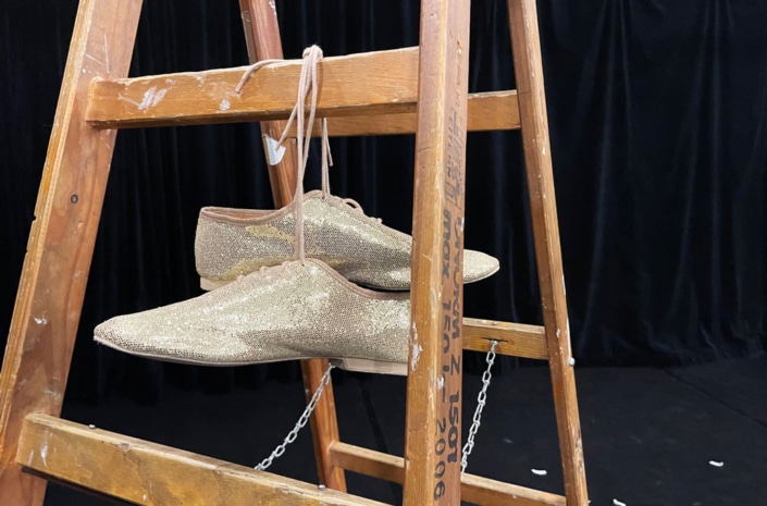 IFANT_Werkraum-Theater01 Große Leiter. An einer Sprosse hängt zusammengebunden ein Paar paillettenbestickter Schuhe